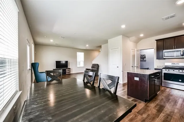 a kitchen with stainless steel appliances granite countertop a stove top oven a sink dishwasher a dining table and chairs with wooden floor