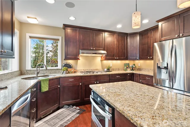 a kitchen with stainless steel appliances granite countertop wooden cabinets a sink a stove a refrigerator and island