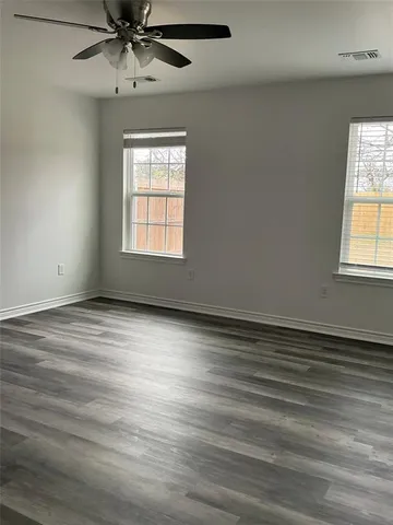 an empty room with wooden floor fan and windows