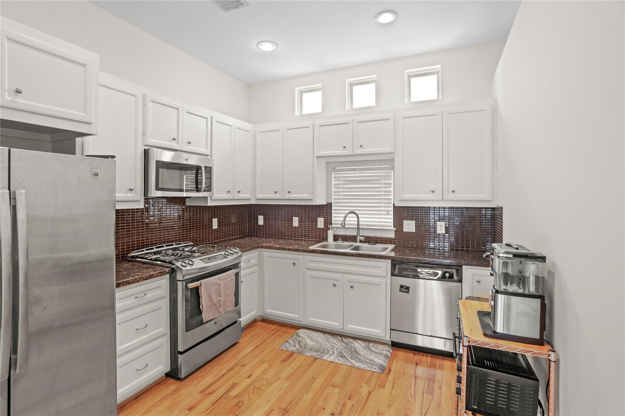 2710 Hullsmith Drive, Unit 604 Houston, TX 77063 - Photo 3 of 27 a kitchen with kitchen island granite countertop a stove top oven a sink dishwasher and white cabinets with wooden floor