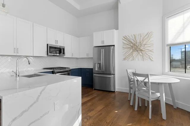 a kitchen with stainless steel appliances a stove a sink a refrigerator white cabinets and a chairs