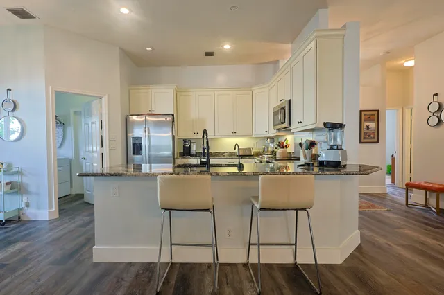 a kitchen with stainless steel appliances granite countertop a refrigerator a stove top oven a sink and island with wooden floor