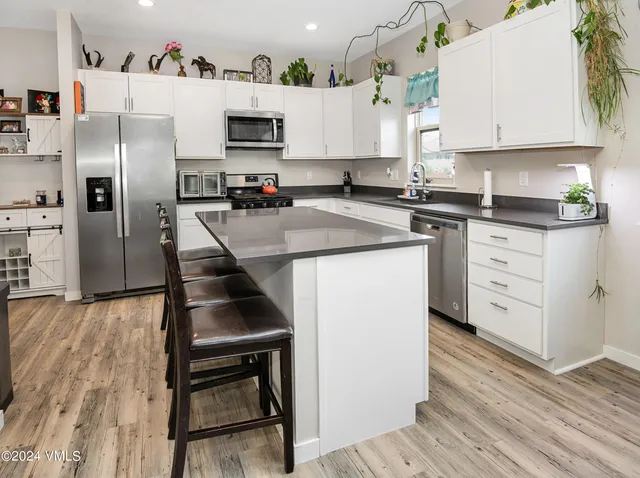 a kitchen with a refrigerator a stove a sink and white cabinets with wooden floor