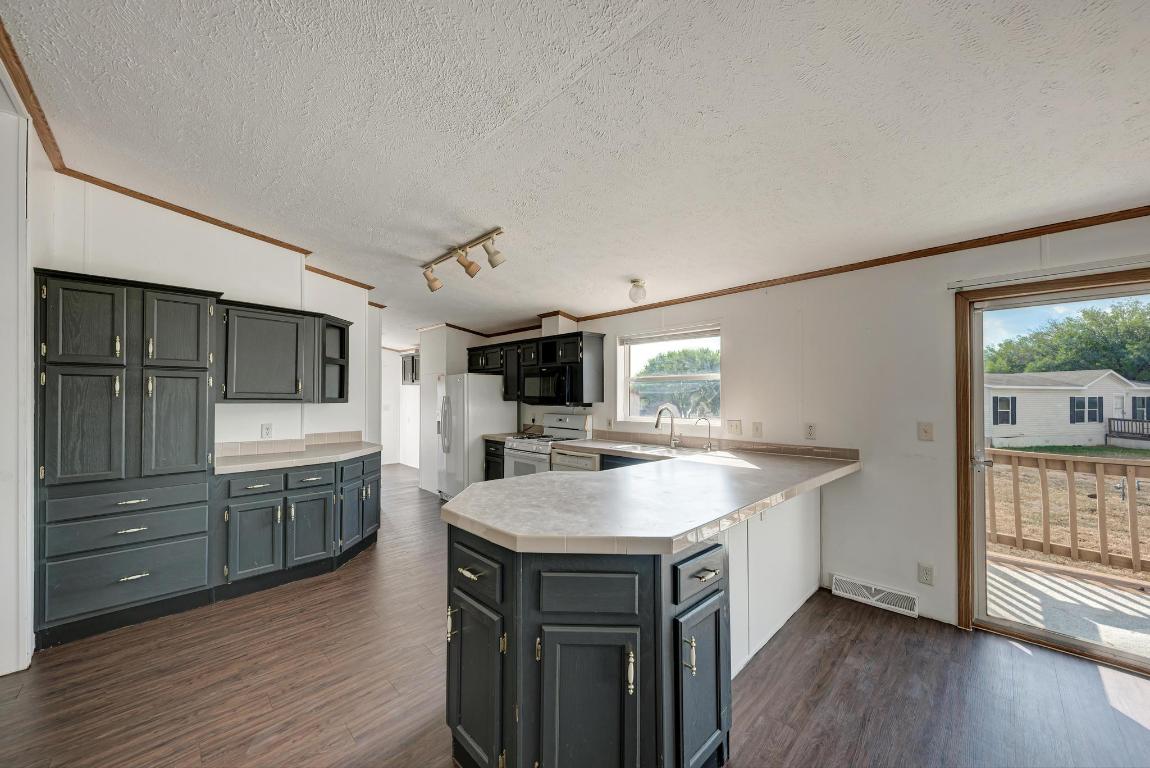 187 Horseshoe Bend Road San Marcos, TX 78666 - Photo 12 of 38 Kitchen featuring ornamental molding, a peninsula, dark wood finished floors, a textured ceiling, and light countertops