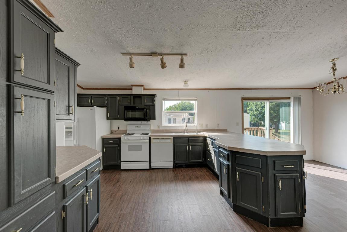 187 Horseshoe Bend Road San Marcos, TX 78666 - Photo 13 of 38 Kitchen featuring a peninsula, white appliances, dark wood-type flooring, ornamental molding, and a textured ceiling
