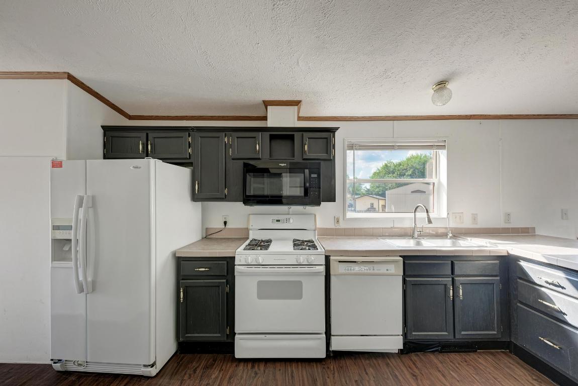 187 Horseshoe Bend Road San Marcos, TX 78666 - Photo 15 of 38 Kitchen featuring white appliances, ornamental molding, dark wood-style floors, light countertops, and a textured ceiling