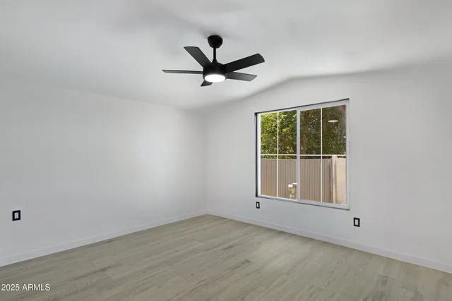 an empty room with wooden floor ceiling fan and windows