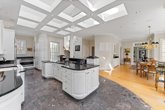 a large white kitchen with granite countertop a stove a sink a window and white cabinets