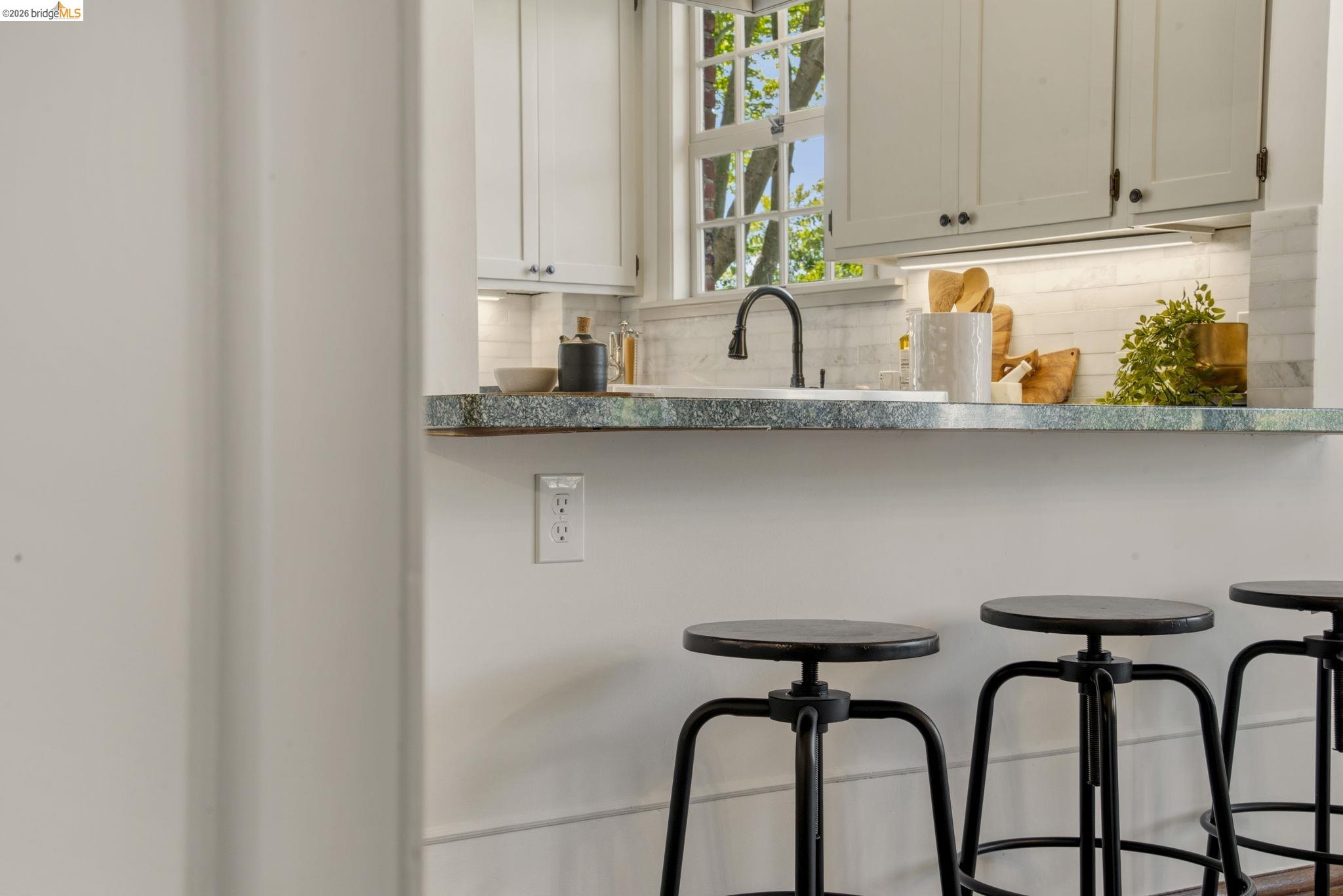 1087 Hubert Road Oakland, CA 94610 - Photo 50 of 67 Kitchen featuring a green patterned countertop, white cabinetry with dark hardware, undermount sink with a black gooseneck faucet, and white subway tile backsplash