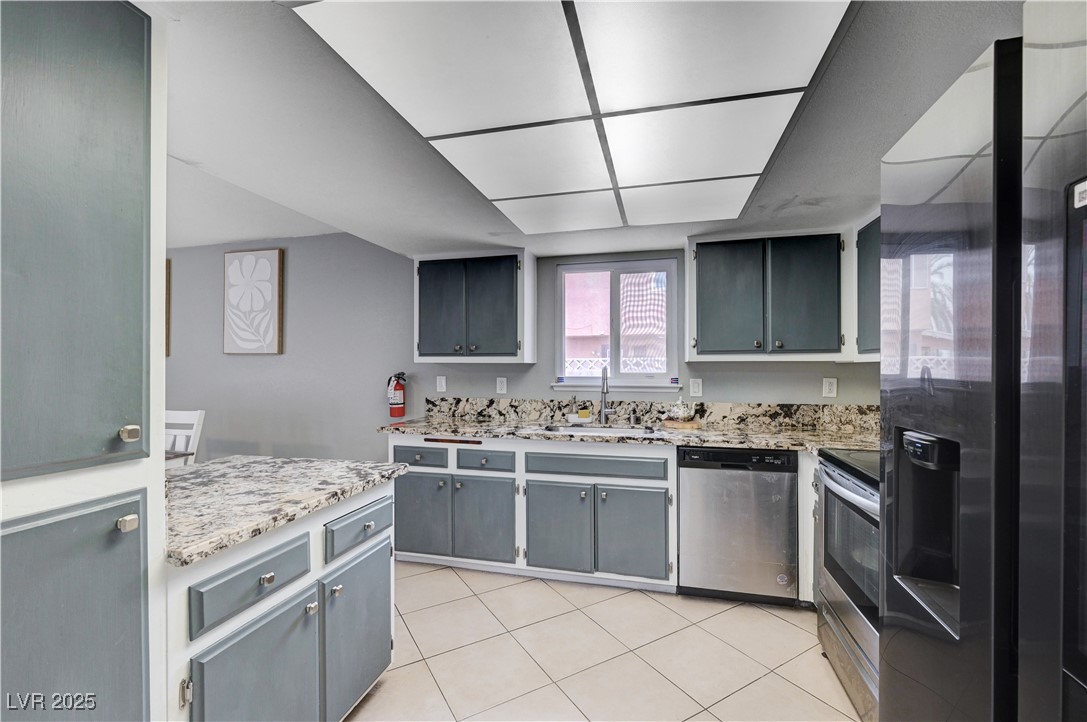 2829 Michael Way Las Vegas, NV 89108 - Photo 35 of 60 Kitchen with gray cabinetry, appliances with stainless steel finishes, light tile patterned floors, and light stone counters