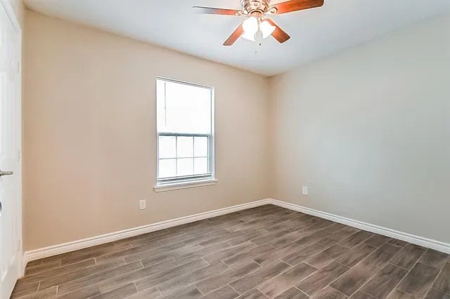 an empty room with wooden floor fan and windows