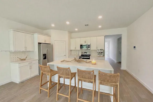 a kitchen with stainless steel appliances kitchen island granite countertop a refrigerator a stove a microwave oven a dining table and chairs with wooden floor