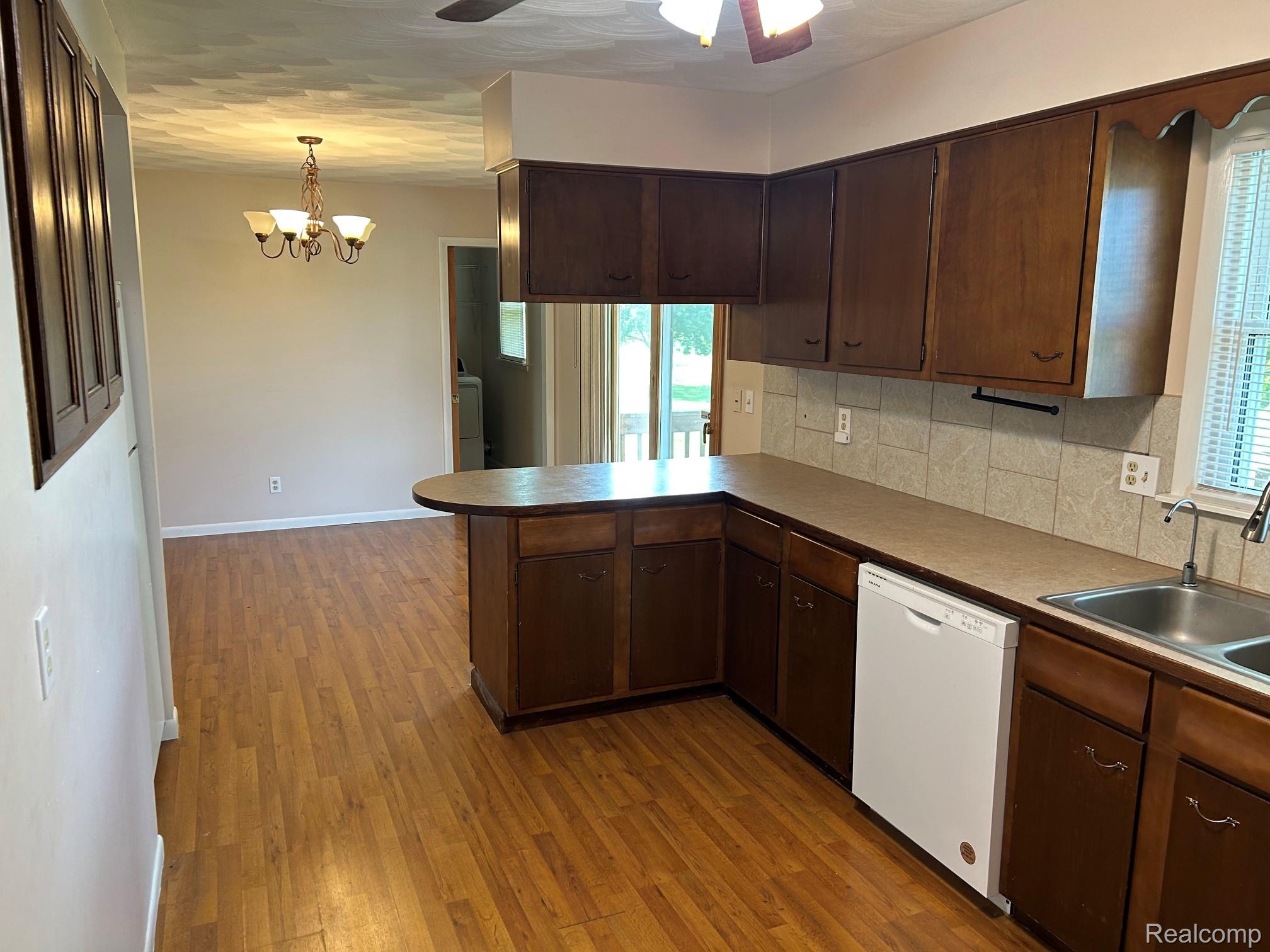 8233 West Iosco Road Fowlerville, MI 48836 - Photo 5 of 7 Spacious kitchen featuring dark wood cabinetry, stainless steel appliances, ceramic tile backsplash, and a curved island with breakfast bar seating