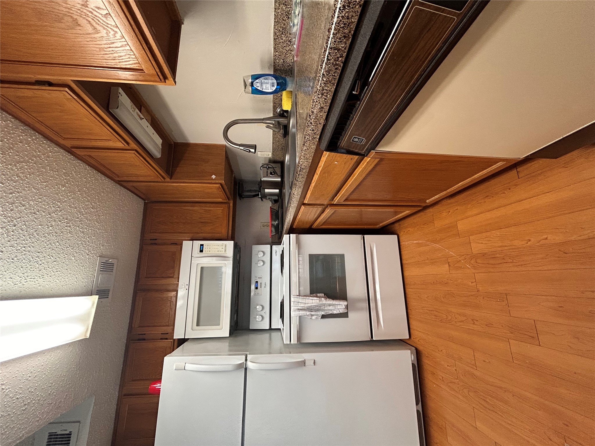 Kitchen featuring white appliances, dark countertops, light wood-style flooring, a textured ceiling, and wood finish cabinets