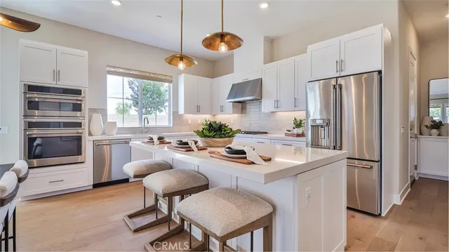 a kitchen with stainless steel appliances kitchen island a table chairs and a refrigerator