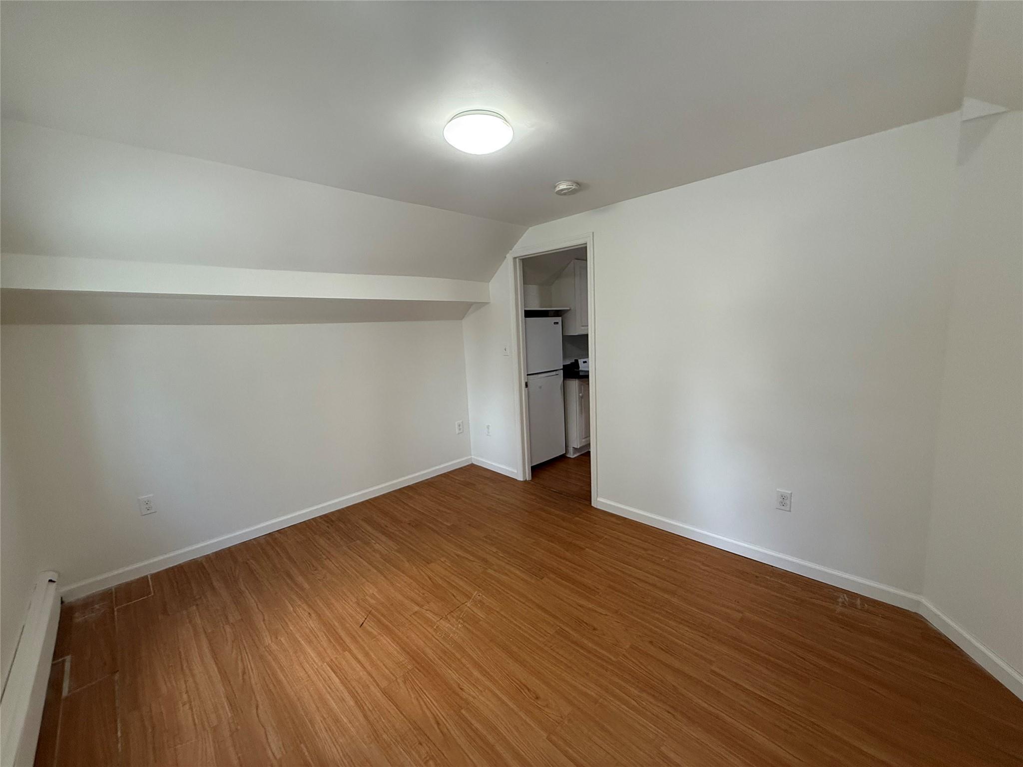 8 Harrison Street, Unit 3 Poughkeepsie, NY 12601 - Photo 5 of 6 Unfurnished bedroom featuring a baseboard radiator, wood finished floors, vaulted ceiling, freestanding refrigerator, and a spacious closet
