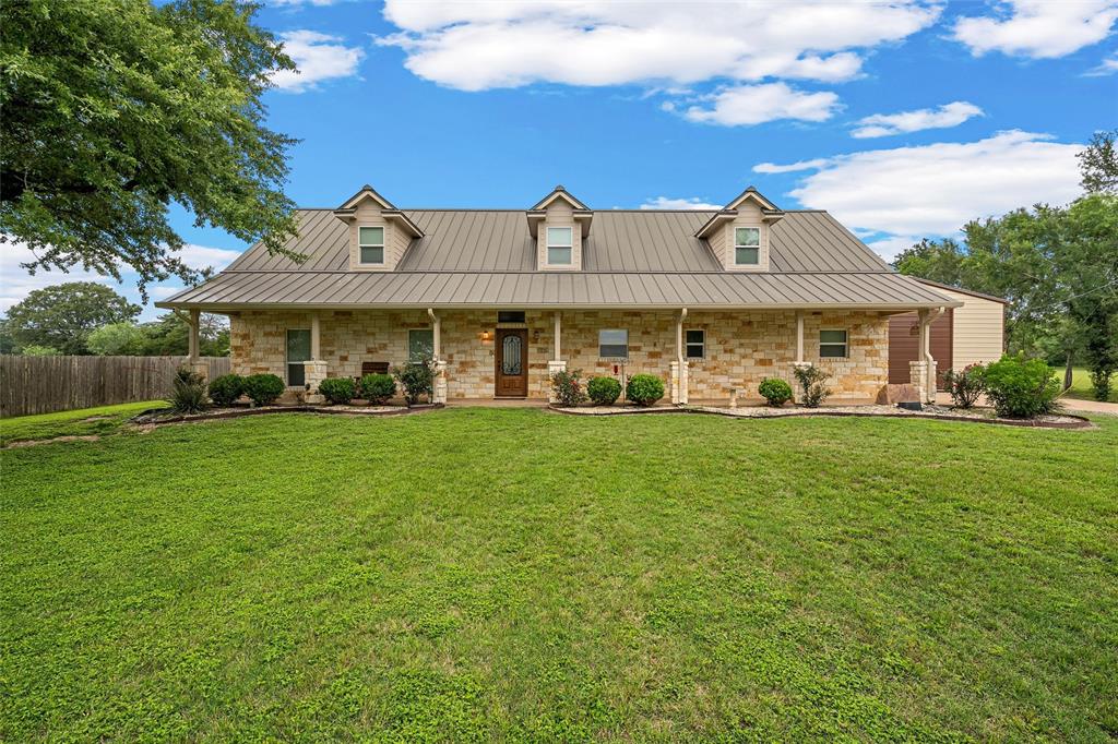 1117 Downsville Road Robinson, TX 76706 - Photo 3 of 40 Stone facade home featuring a standing seam metal roof, covered front porch with columns, multiple dormer windows, and a wood-paneled entry door