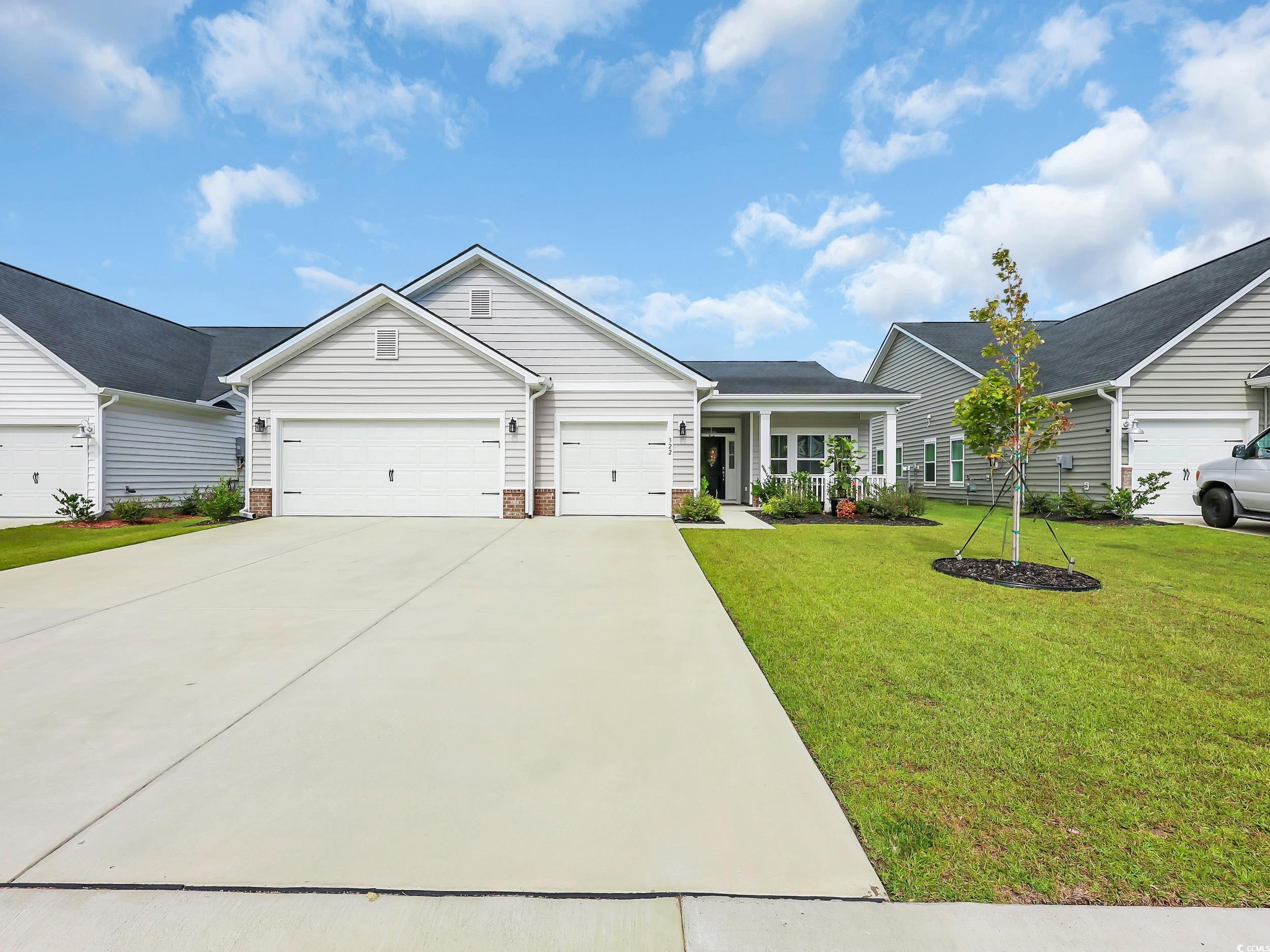 Ranch-style home featuring a porch, driveway, a garage, a front lawn, and brick siding