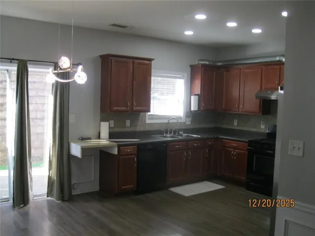 a kitchen with stainless steel appliances granite countertop wooden cabinets a stove a sink and dishwasher with wooden floor