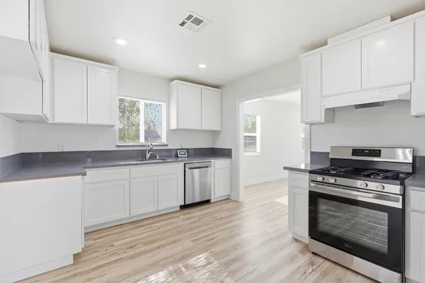 a kitchen with granite countertop wooden floor stainless steel appliances and white cabinets