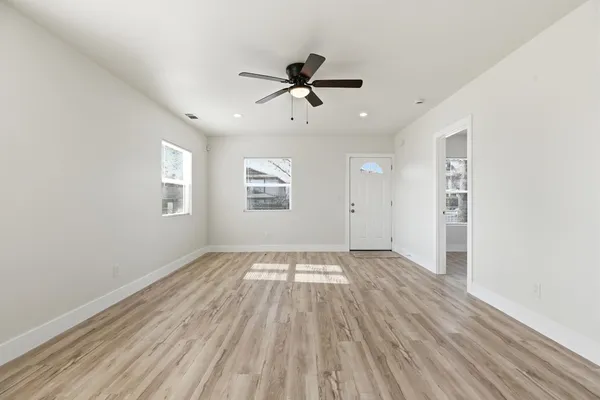 an empty room with wooden floor a ceiling fan and windows