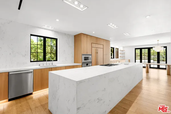 a large white kitchen with kitchen island a large counter top space a sink a window and stainless steel appliances