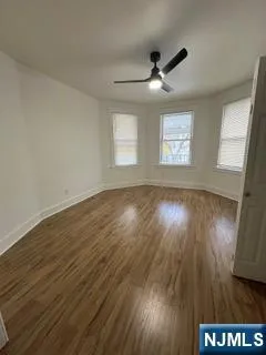 an empty room with wooden floor fan and windows