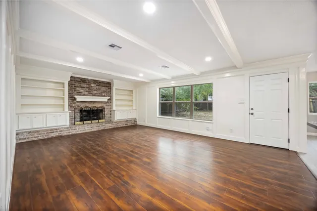 an empty room with wooden floor fire place and windows