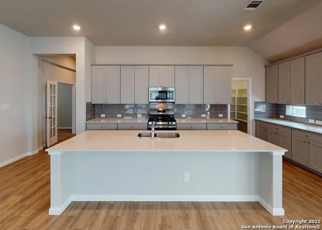 a large white kitchen with kitchen island a sink dishwasher a refrigerator and a stove with wooden floor