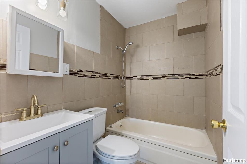 26076 Colgate Street Inkster, MI 48141 - Photo 15 of 24 Bathroom featuring a tiled shower surround with a decorative accent band, a white drop-in bathtub, and a vanity with a white rectangular sink and brass-finish faucet