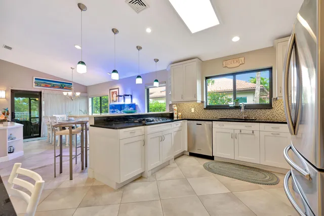 a kitchen with stainless steel appliances kitchen island granite countertop a refrigerator a sink a stove and white cabinets with wooden floor