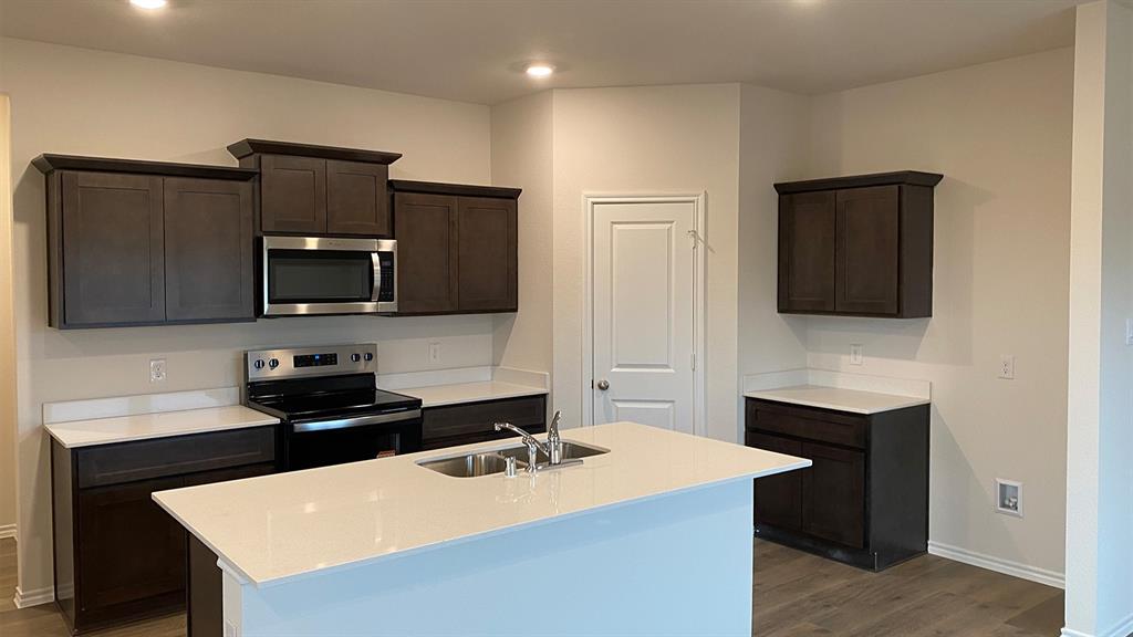 107 Hunters Way Canton, TX 75103 - Photo 22 of 23 Kitchen featuring dark wood finish cabinets, stainless steel appliances, a kitchen island with sink, light stone counters, and dark wood-style flooring