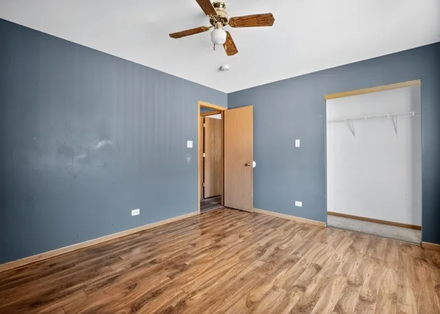 a view of an empty room with wooden floor and a ceiling fan