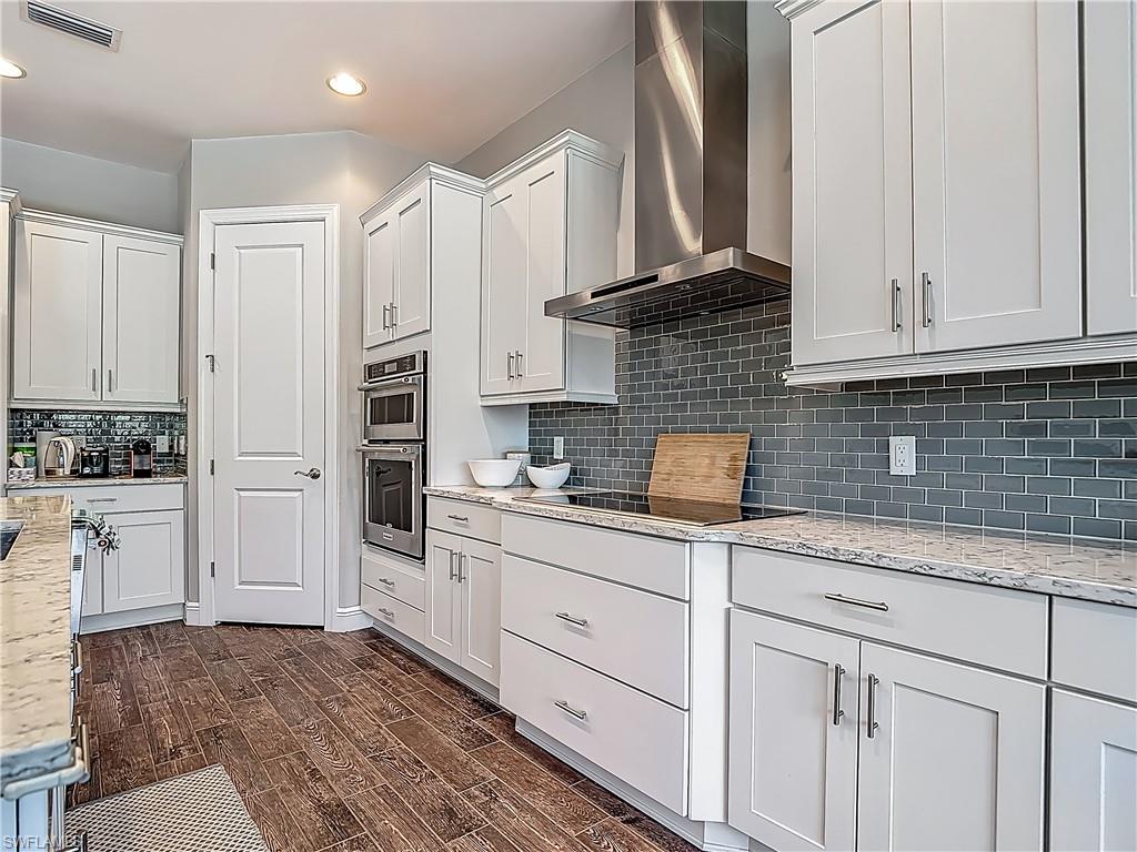 4524 Tamarind Way Naples, FL 34119 - Photo 10 of 50 Kitchen featuring wall chimney range hood, white cabinetry, dark wood finished floors, recessed lighting, and tasteful backsplash
