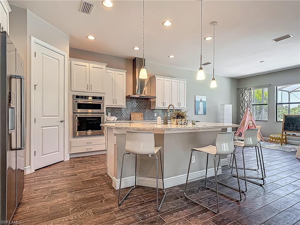 4524 Tamarind Way Naples, FL 34119 - Photo 13 of 50 Kitchen featuring wall chimney exhaust hood, appliances with stainless steel finishes, dark wood-type flooring, a breakfast bar, and recessed lighting