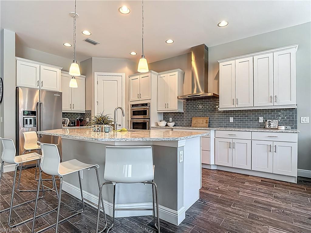 4524 Tamarind Way Naples, FL 34119 - Photo 14 of 50 Kitchen featuring wall chimney exhaust hood, stainless steel appliances, a breakfast bar, a kitchen island with sink, and recessed lighting