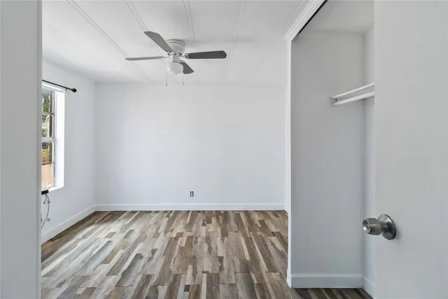 an empty room with wooden floor and a ceiling fan