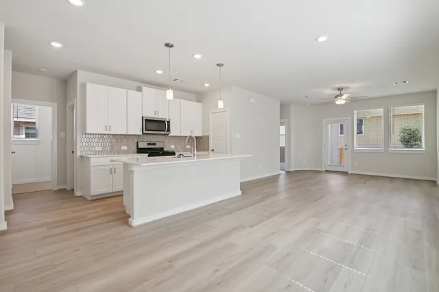 an empty room with wooden floor chandelier fan and windows