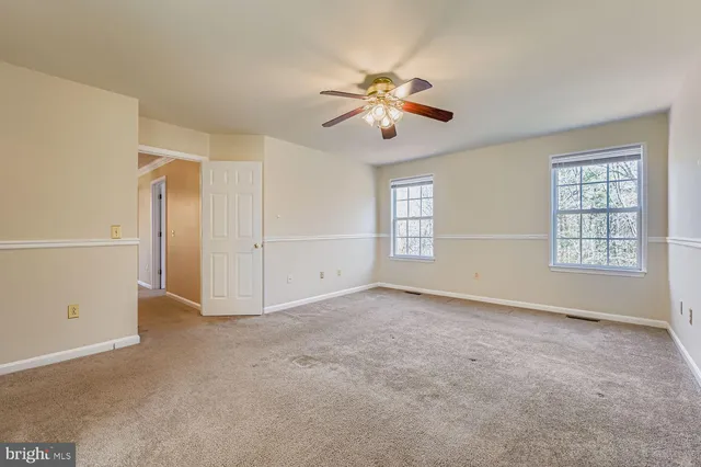 a view of an empty room with chandelier fan and windows