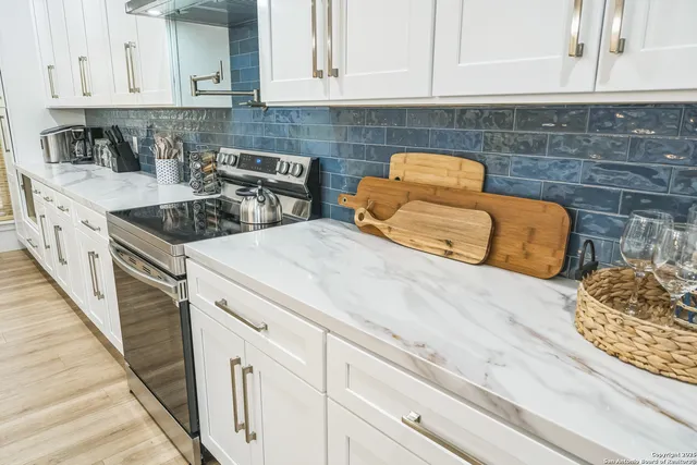 a kitchen with granite countertop a stove a sink and white cabinets
