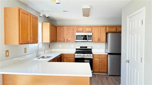 a kitchen with stainless steel appliances a stove a sink a refrigerator white cabinets and wooden floor