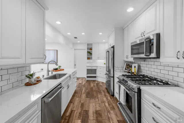 a kitchen with stainless steel appliances a stove top oven a sink a refrigerator white cabinets and wooden floor