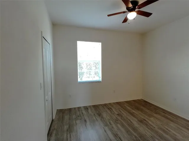 an empty room with wooden floor fan and windows