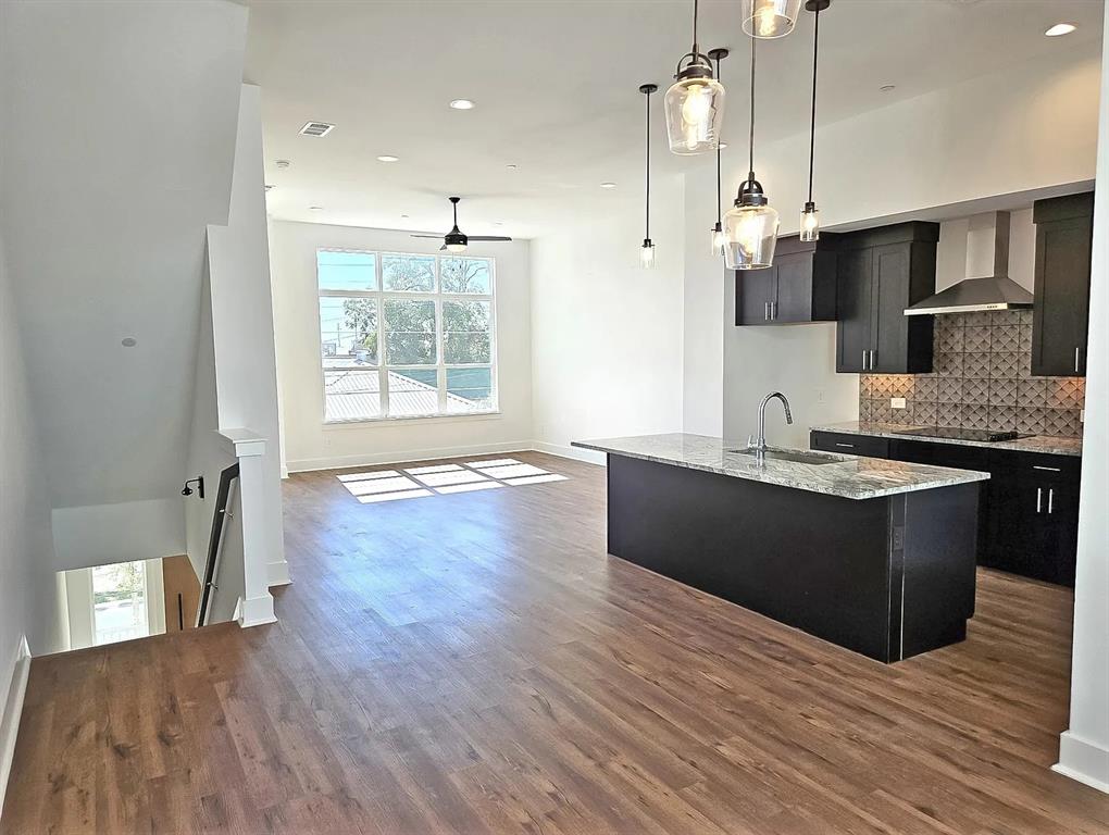13325 Bee Street, Unit 406 Farmers Branch, TX 75234 - Photo 30 of 30 Kitchen with dark cabinets, a kitchen island with sink, decorative backsplash, open floor plan, and wall chimney exhaust hood