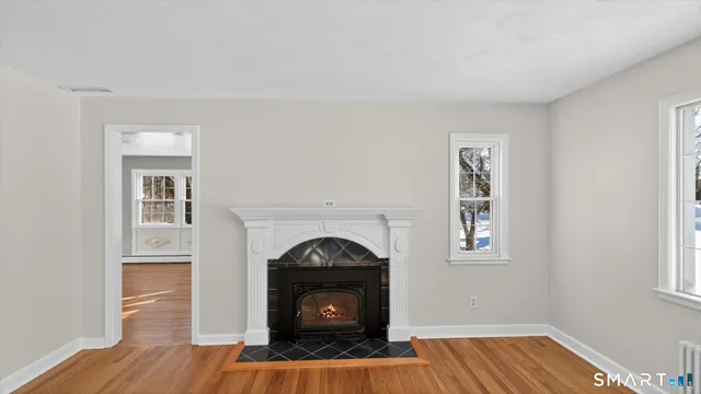a view of an empty room with wooden floor fireplace and a window