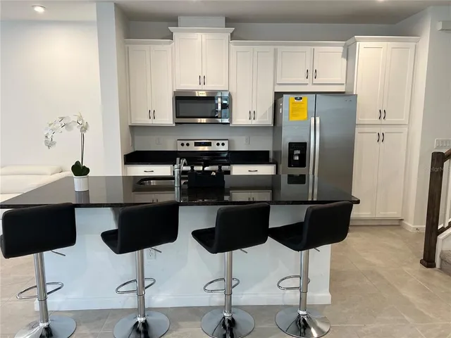 a kitchen with stainless steel appliances kitchen island a refrigerator a stove a sink and chairs with wooden floor