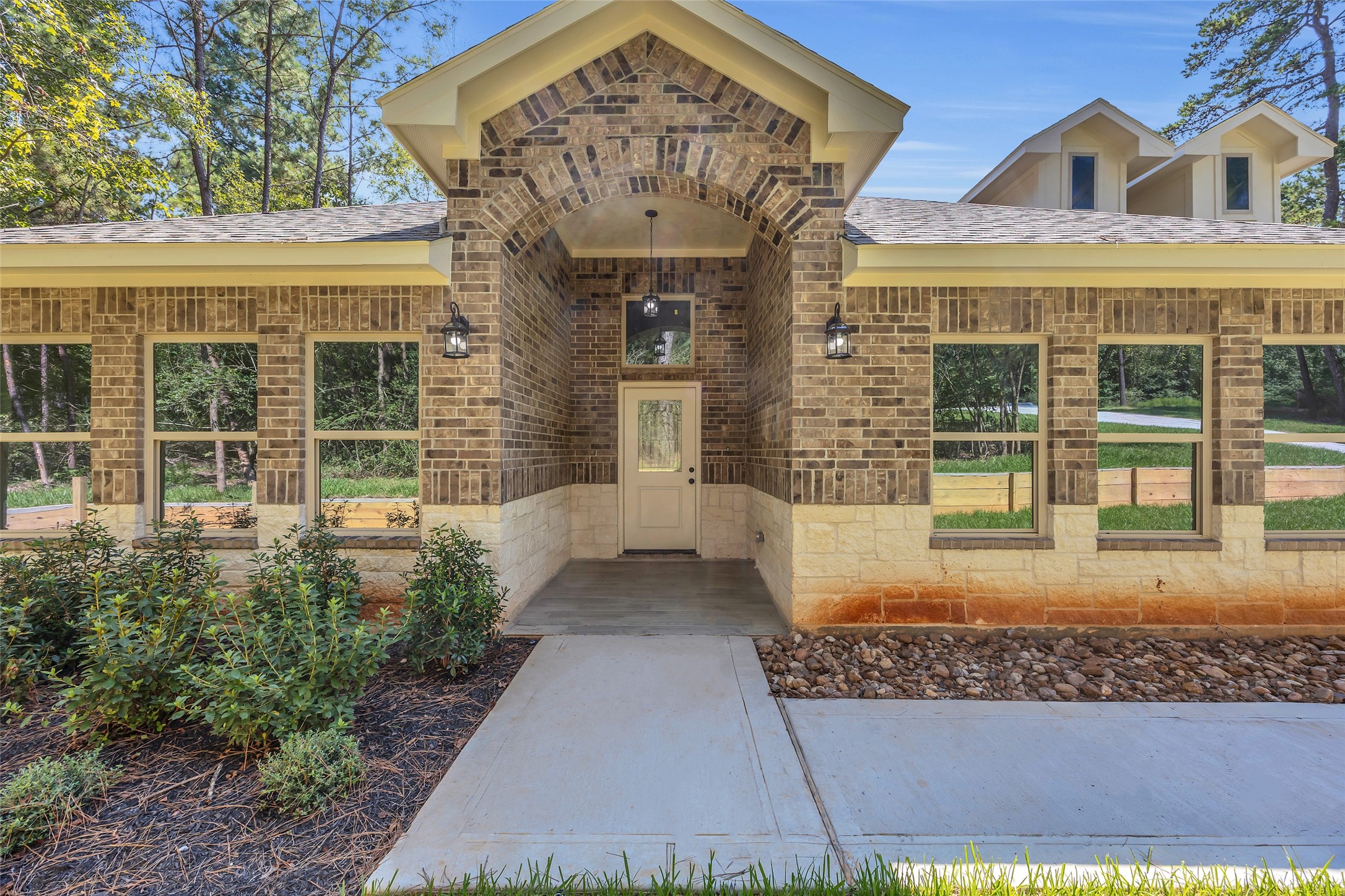 162 Bighorn Road Huntsville, TX 77340 - Photo 1 of 48 This photo showcases a modern brick home with a welcoming front entrance, featuring a covered porch and large windows. The house has a landscaped garden and set in a wooded area, offering a serene and private setting.