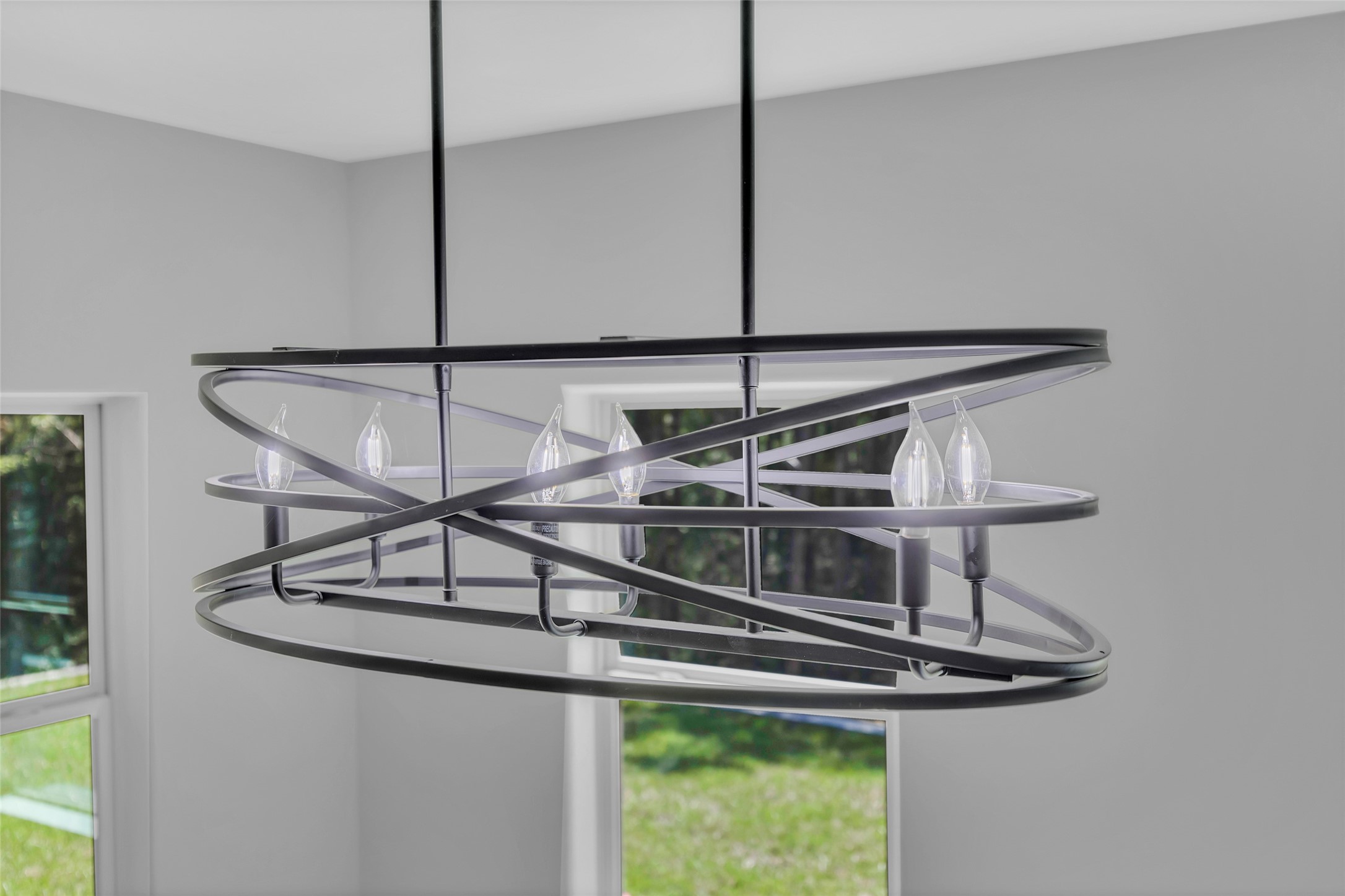 162 Bighorn Road Huntsville, TX 77340 - Photo 16 of 48 Modern chandelier with a sleek, geometric design featuring multiple light bulbs. It hangs in a bright room with large windows, offering a view of green outdoor scenery.