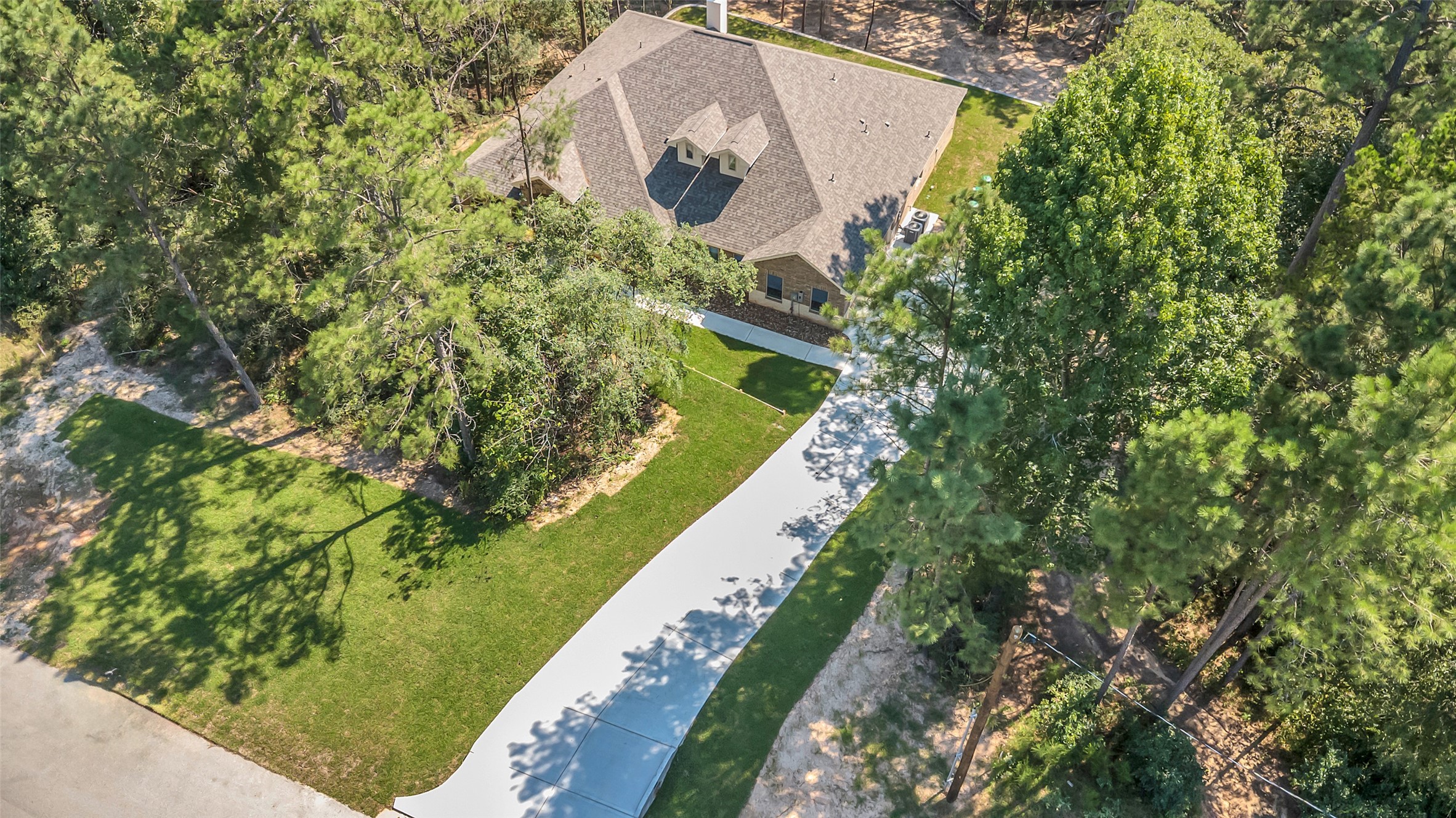 162 Bighorn Road Huntsville, TX 77340 - Photo 43 of 48 This aerial view showcases a charming home nestled among mature trees. It features a long driveway, a well-maintained lawn, and is surrounded by lush greenery, offering a sense of privacy and tranquility.