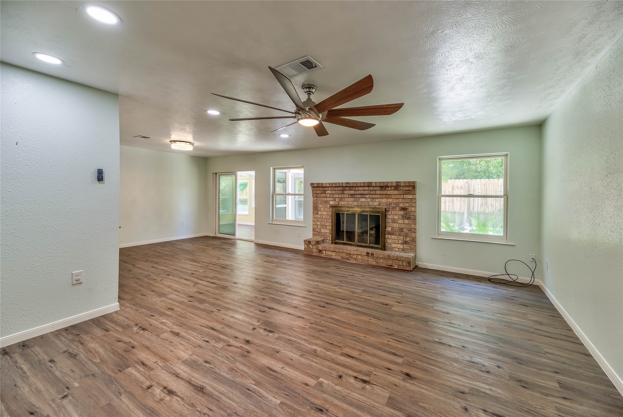 3003 Paul Knox Street Huntsville, TX 77320 - Photo 5 of 46 an empty room with wooden floor a ceiling fan a fireplace and windows